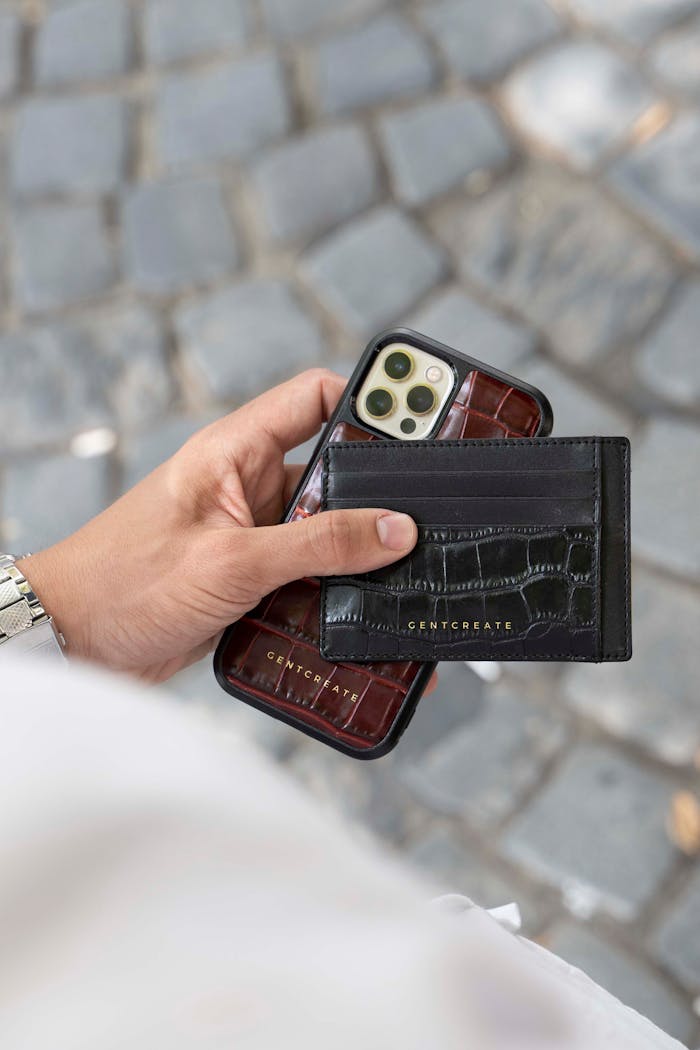 services-04 Person holding an iPhone with a black leather card holder on a paved street.